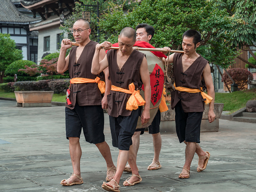 Men in traditional Chinese dress carrying a large crock of vinegar