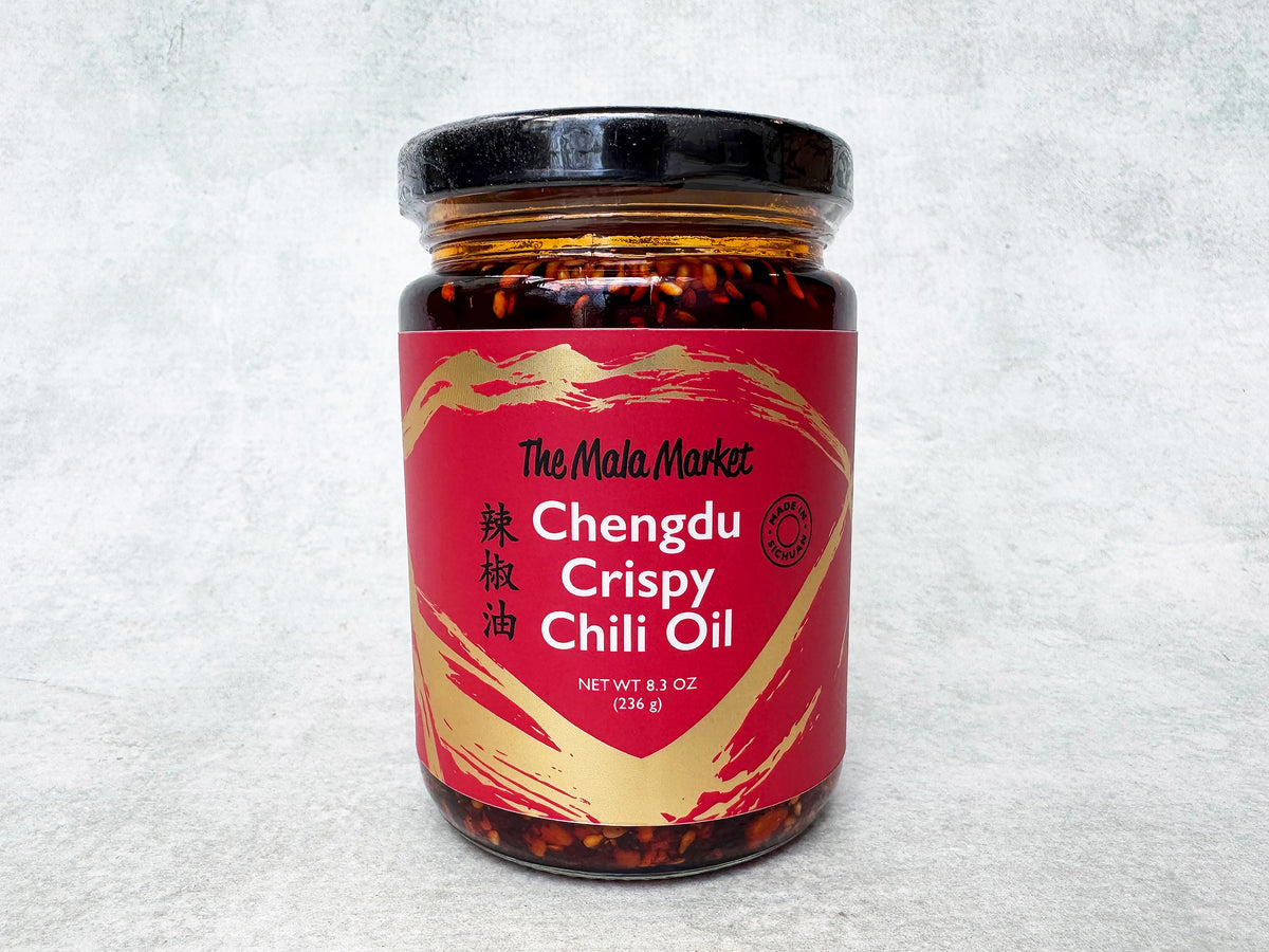 A glass jar of Chengdu Crispy Chili Oil by The Mala Market, with a red label and visible chili crisp on the top. 