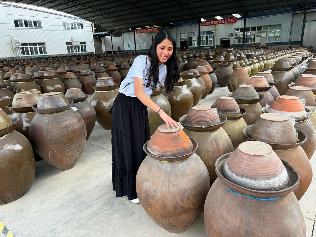 a woman in a fermented soybean factory standing among traditional earthenware crocks of Tongchuan fermented black beans
