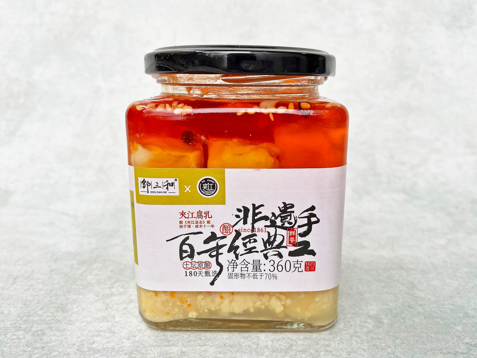 a square glass jar with cubes of tofu in an oil that is red on top and clear on the bottom half of the jar, with a label that has Chinese characters