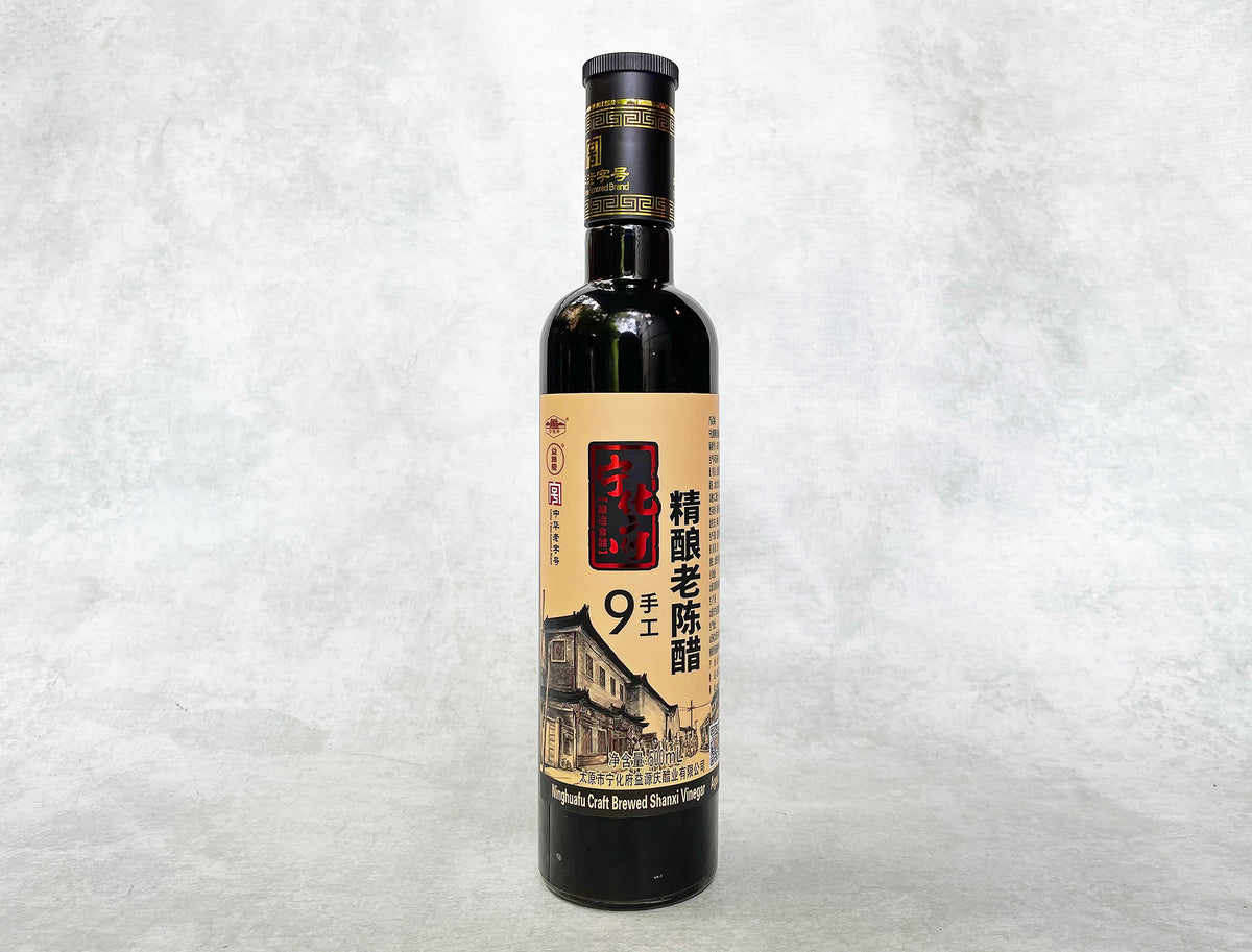 a glass bottle of black Shanxi vinegar with a beige and red metallic label showing an old workshop