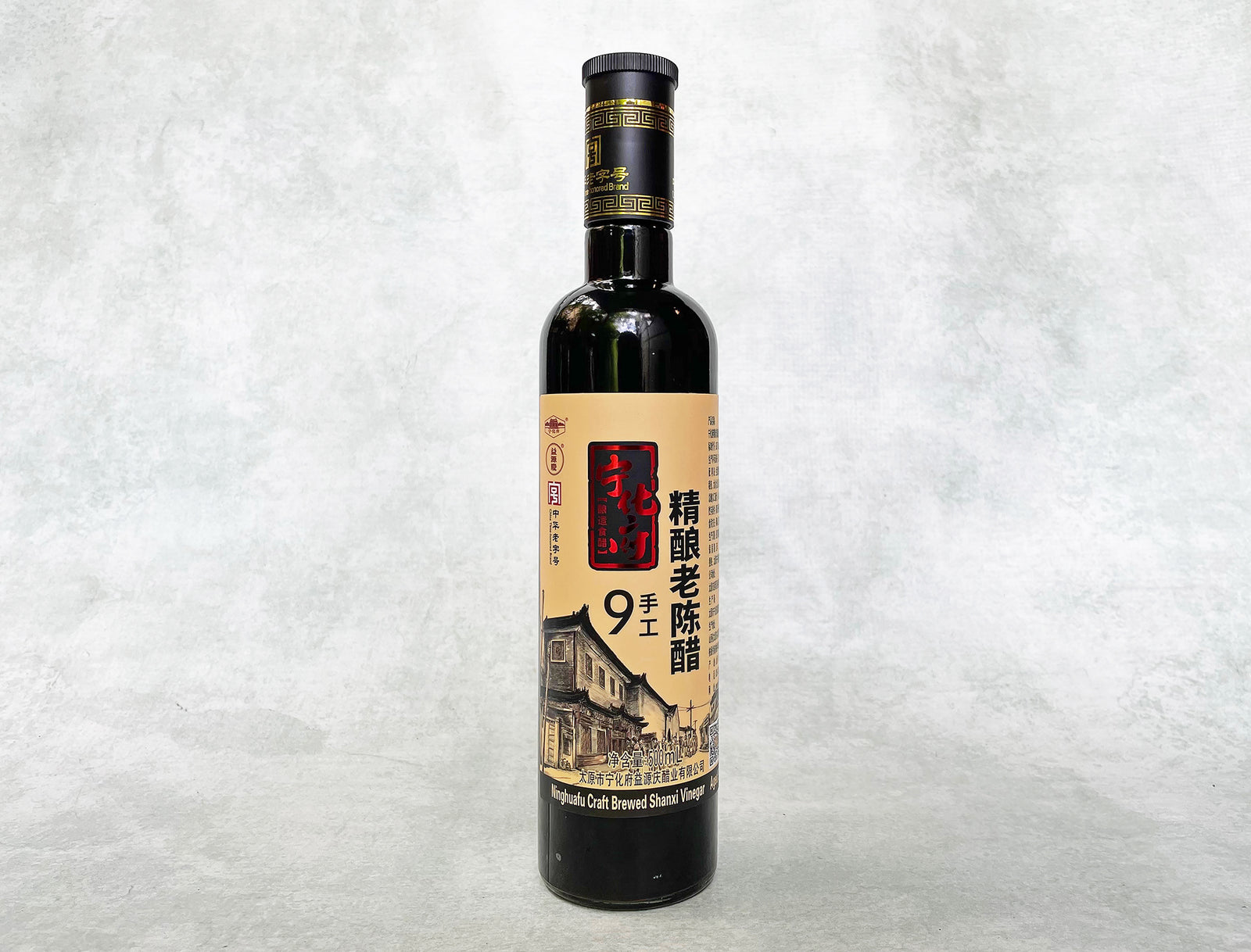 a glass bottle of black Shanxi vinegar with a beige and red metallic label showing an old workshop