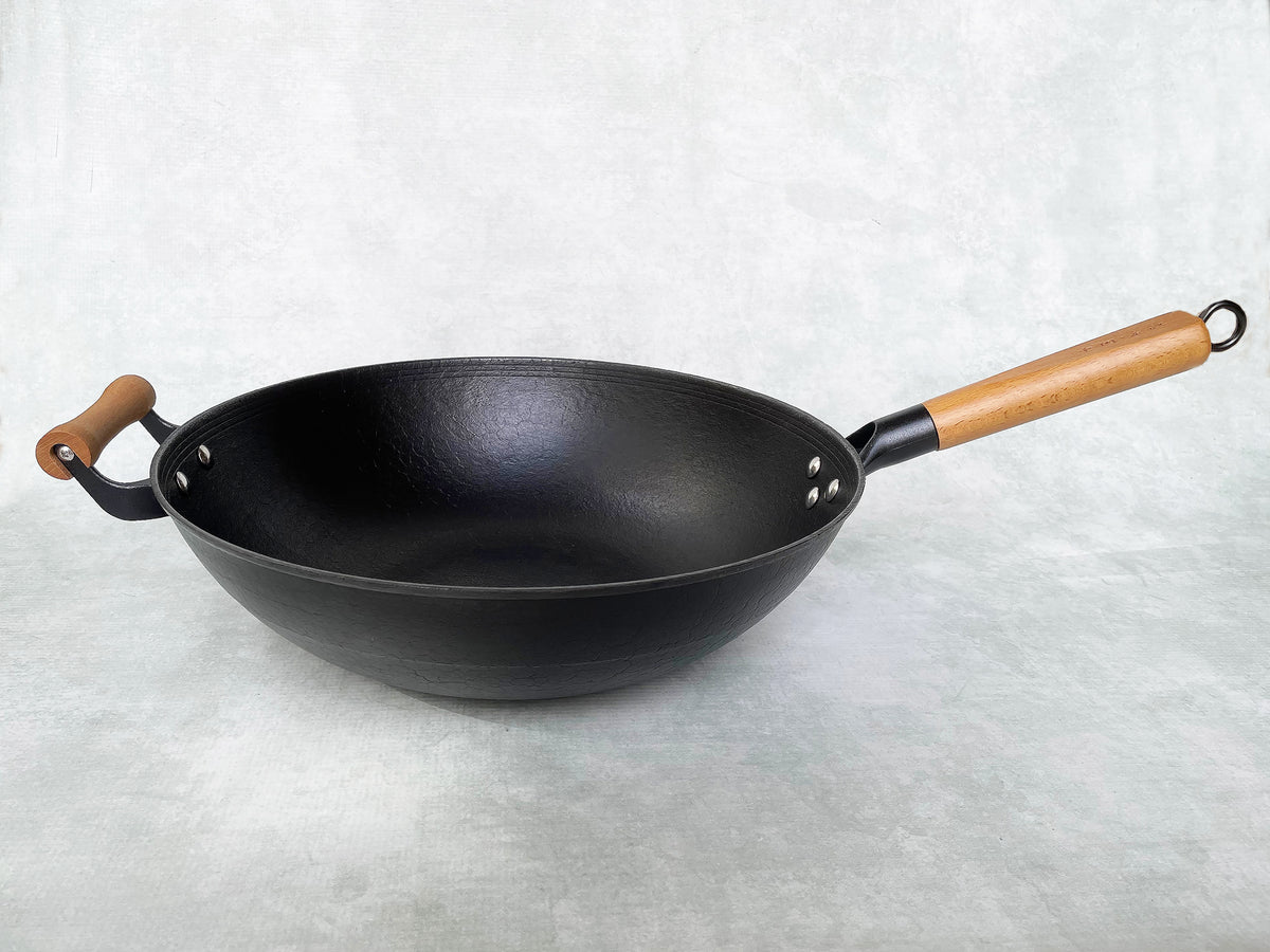 side view of a 14 inch cast iron wok with long wood handle and short wood helper handle