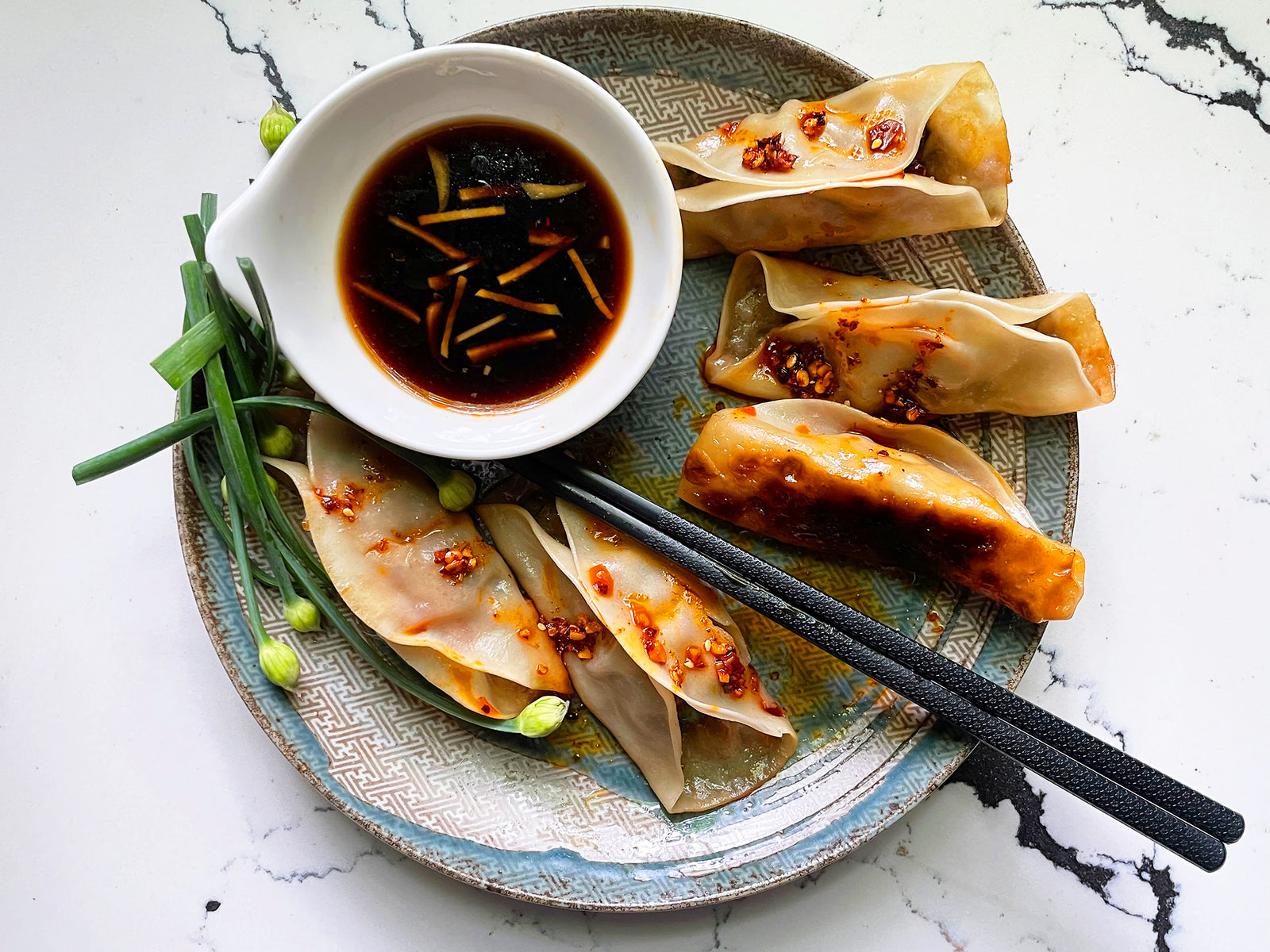 Potstickers on a plate with chopsticks and a bowl of vinegar dipping sauce