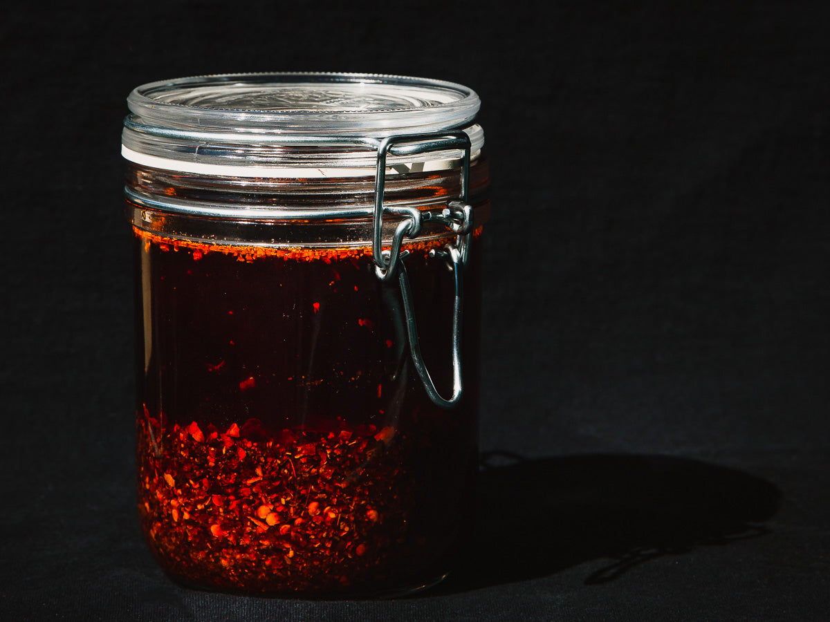 A glass jar of red chili oil with crisp in the bottom and a latch lid