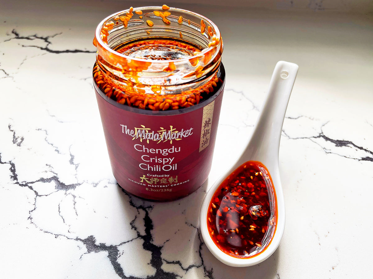 a jar of Chengdu Crispy Chili Oil with the lid off, showing the contents, and a spoonful of the red oil next to it