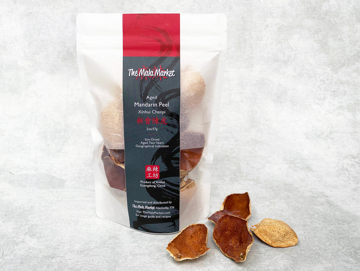 a white kraft bag of aged mandarin peel with a few pieces of dark-orange peel displayed beside it