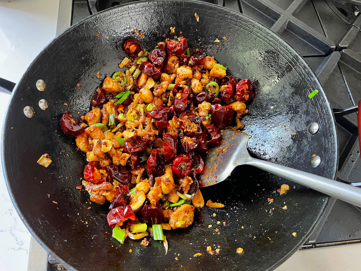 a dish of fried chicken and chilies in a cast iron wok with a spatula