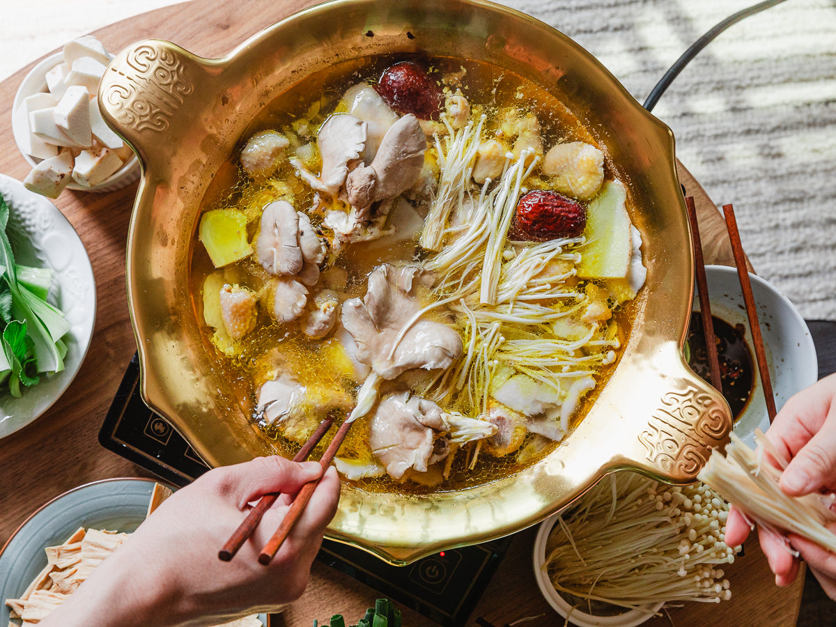 gold stainless steel hot pot full of mushrooms and soup with small bowls of ingredients