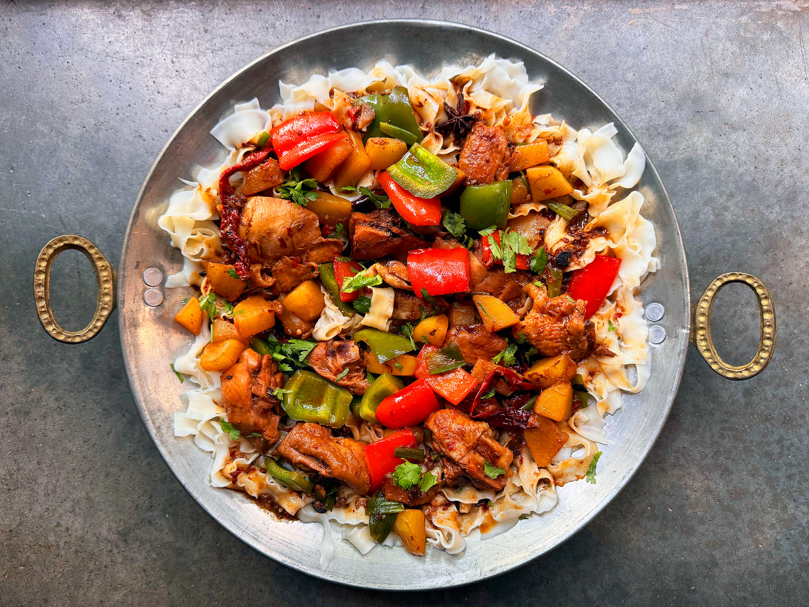 a large metal platter of knife-cut noodles covered with a chicken and pepper stew
