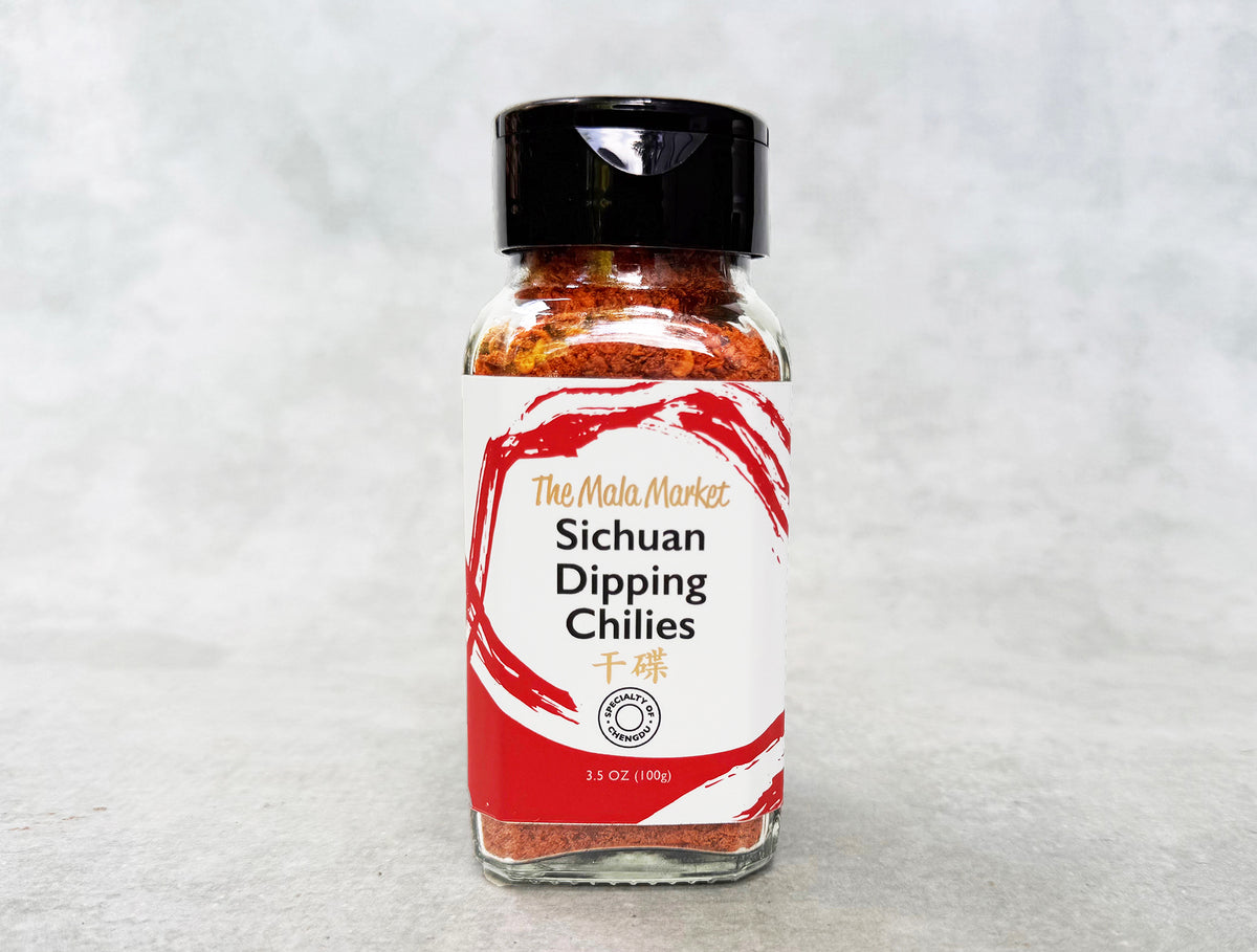 a glass jar of mixed red chilies and spices with a black cap