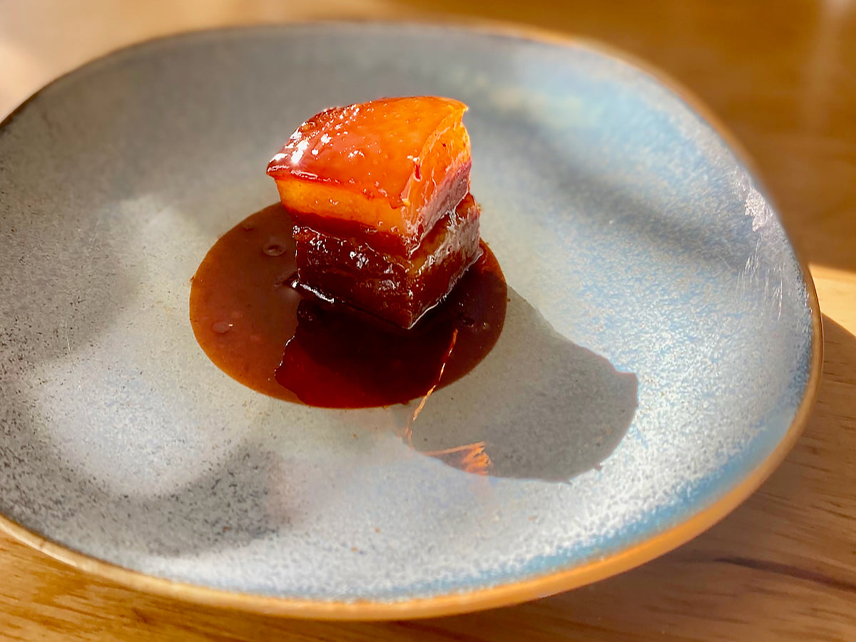 A piece of red-cooked pork belly on a blue plate