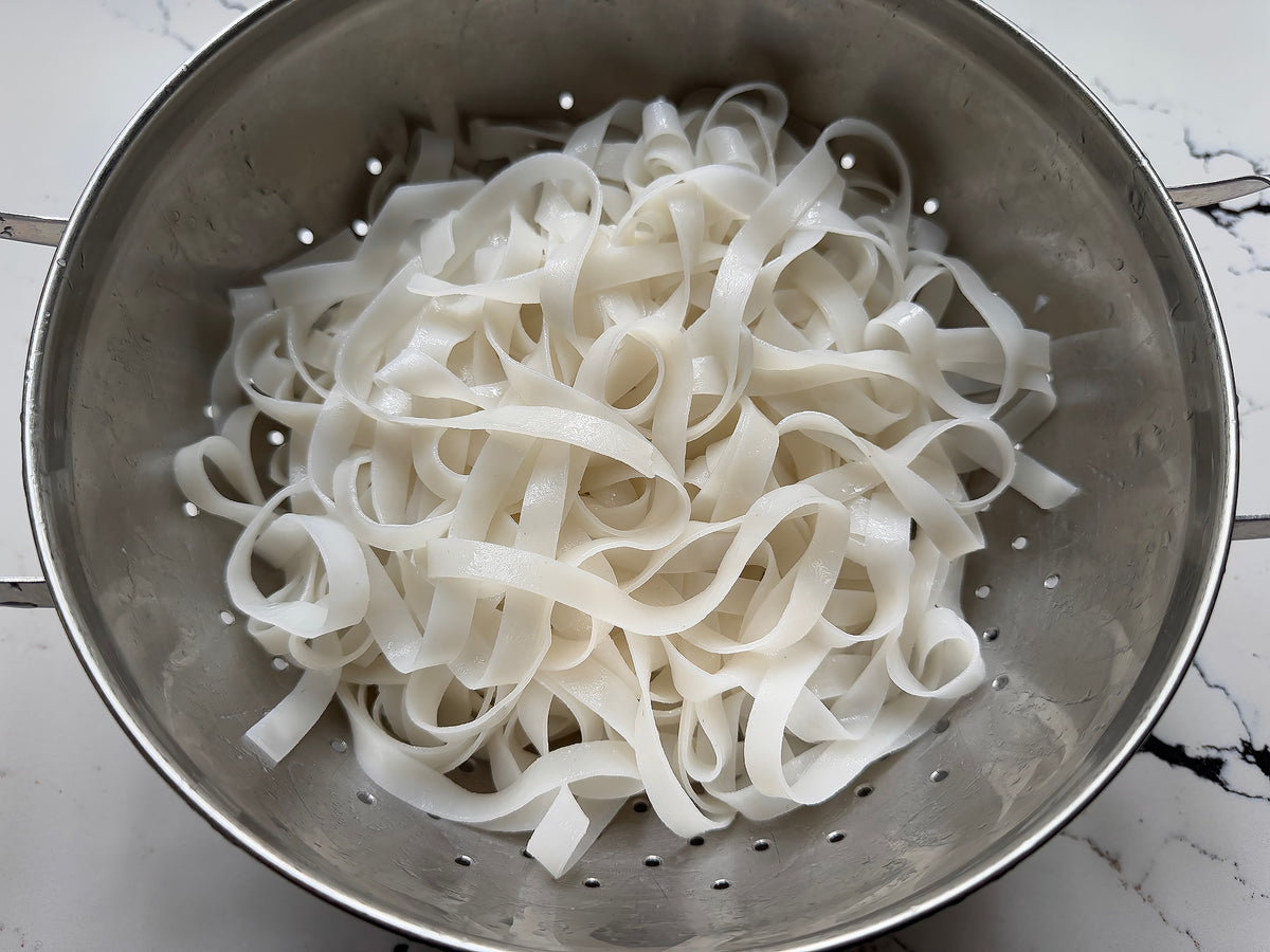 A colander of dried rice noodles that have been soaked and rehydrated