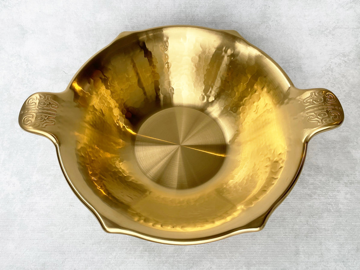 Angled view of a gold stainless steel hot pot with hammered interior and flat bottom. 