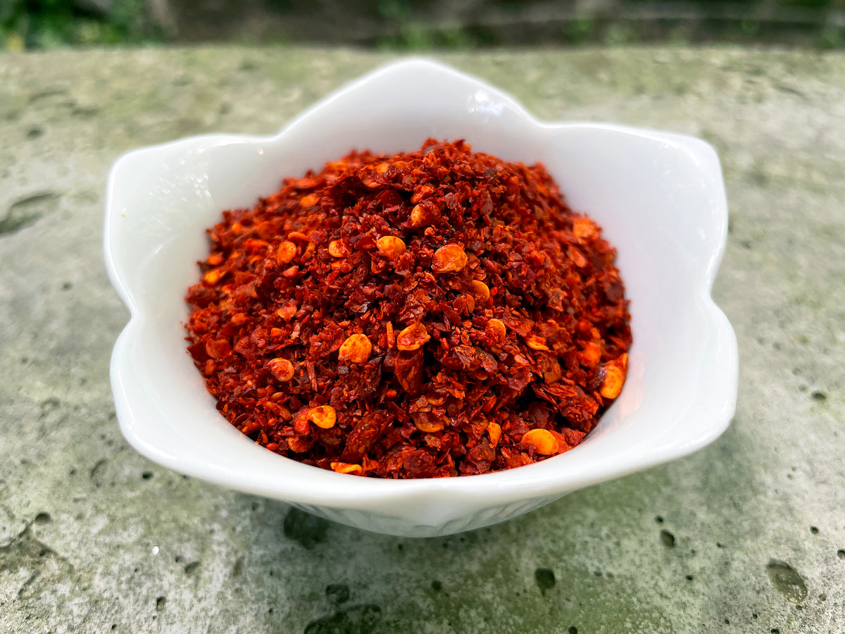 a closeup of a small white bowl of red ground chilies showing flakes, powder and seeds