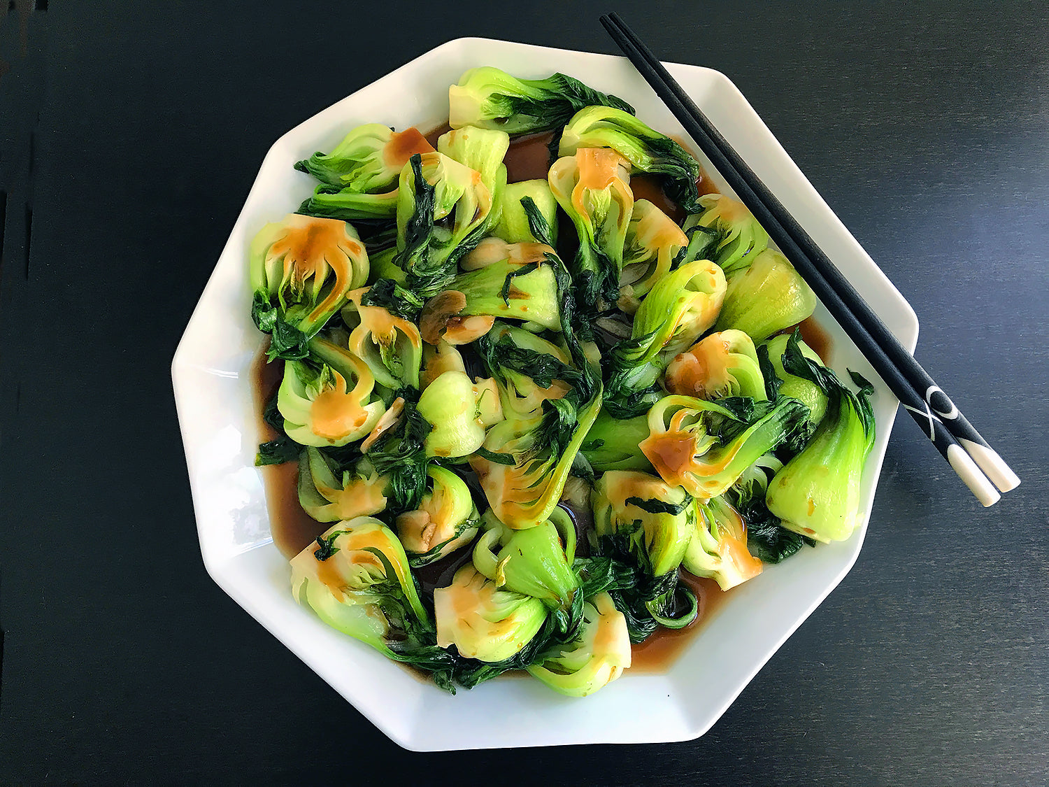 Stir-fried baby bok choy in a brown sauce on a white plate