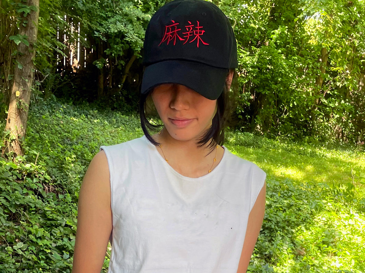 a young Asian woman wearing a black cap with the Chinese characters for mala embroidered on the front in red
