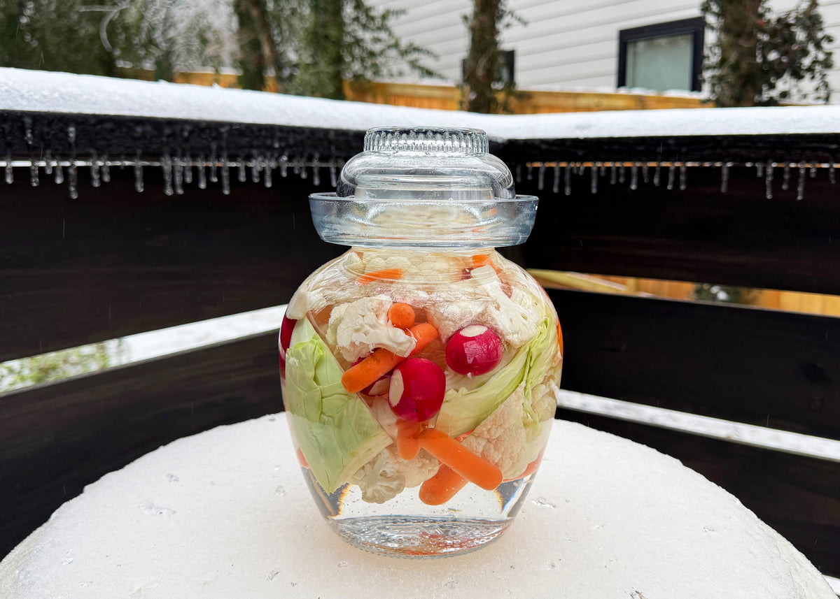 a glass pickle jar filled with vegetables on a snowy table
