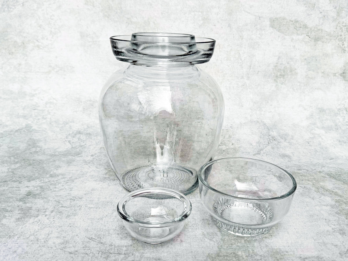 a glass pickle jar with its glass cap and glass insert shown beside it