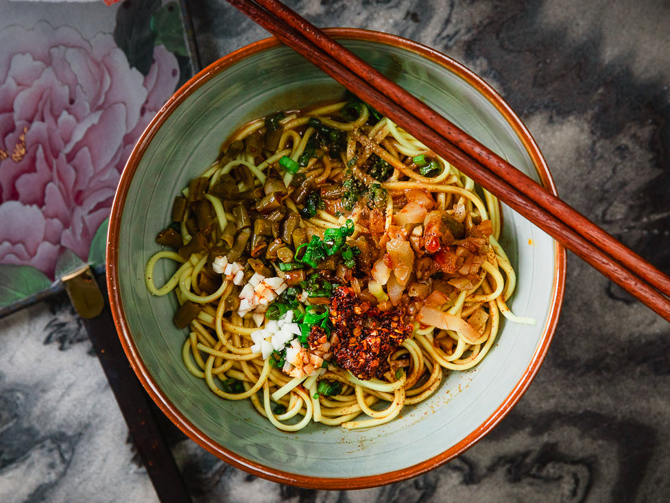 A bowl of Wuhan hot dry noodles with sesame sauce and pickled green beans