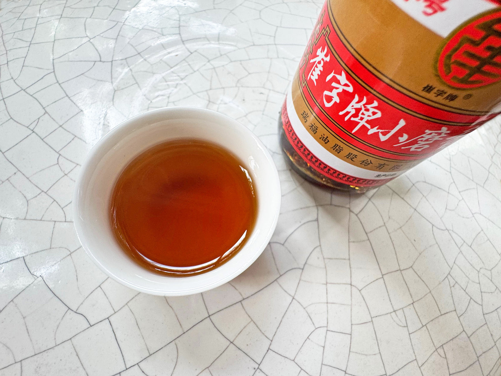 A small cup of golden sesame oil next to the bottle of sesame oil