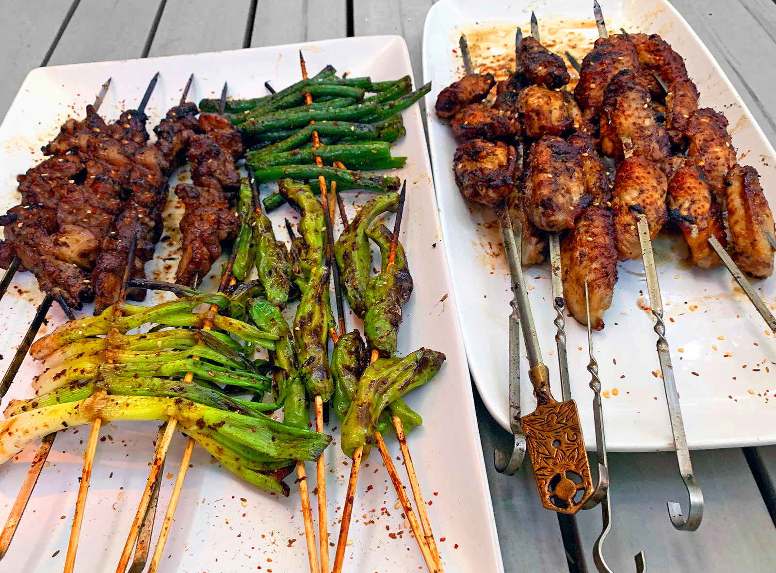 Skewers of grilled meat and vegetables covered in Sichuan spice on a white plate 