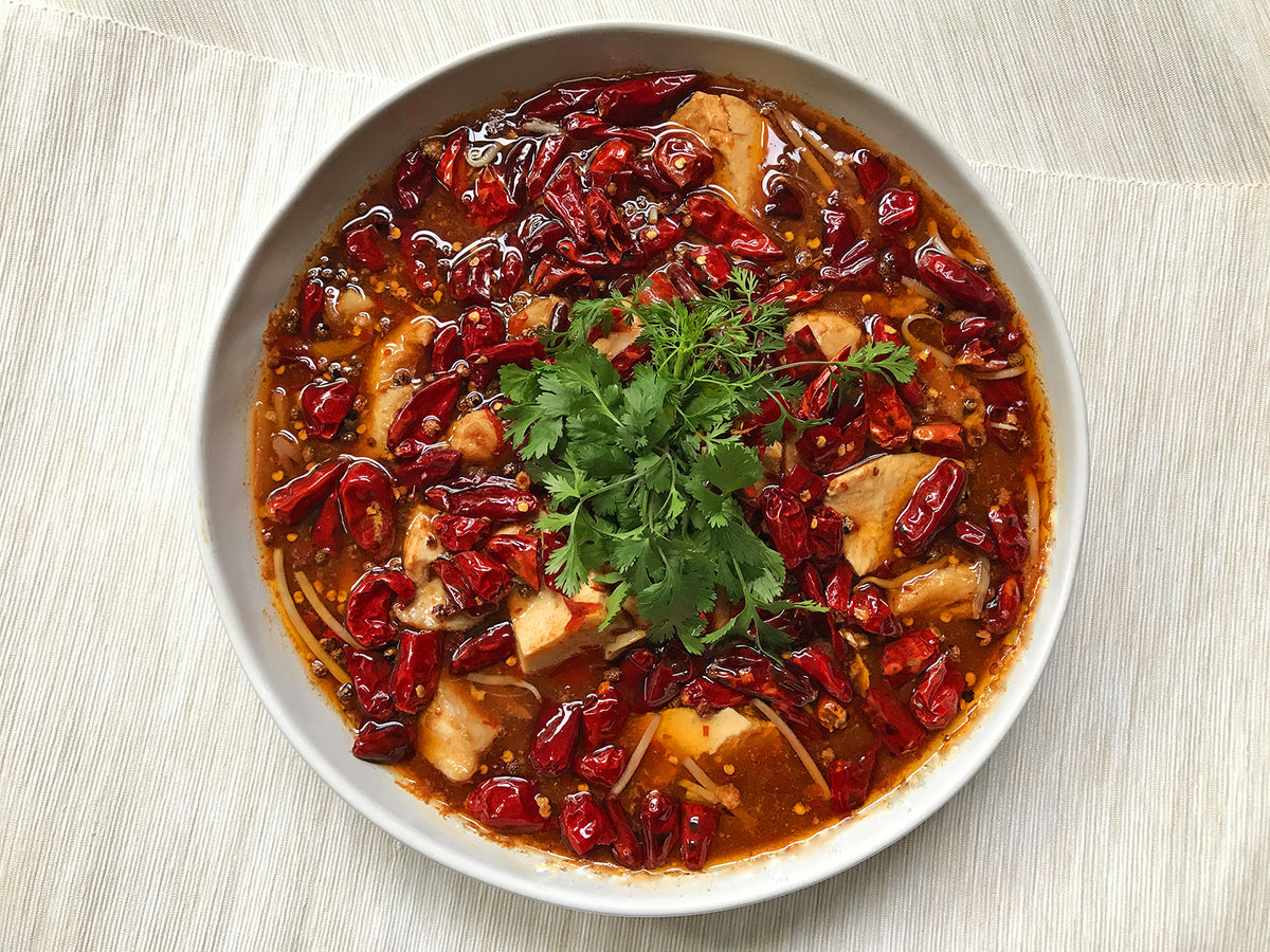 A bowl of fish and tofu in a spicy red brown sauce with chilies