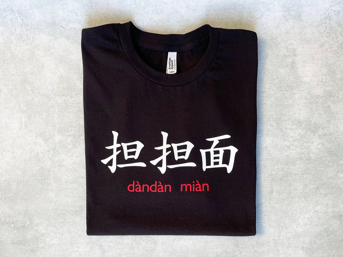 A black folded t-shirt with the text '担担面 dan dan mian in white.