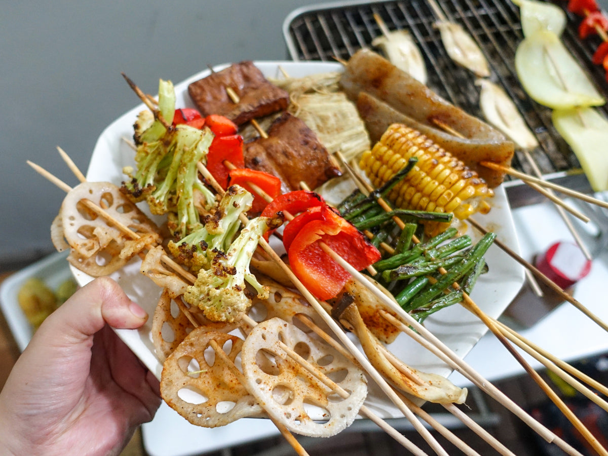 A plate of various vegetable skewers fresh off the grill, with the grill in the background