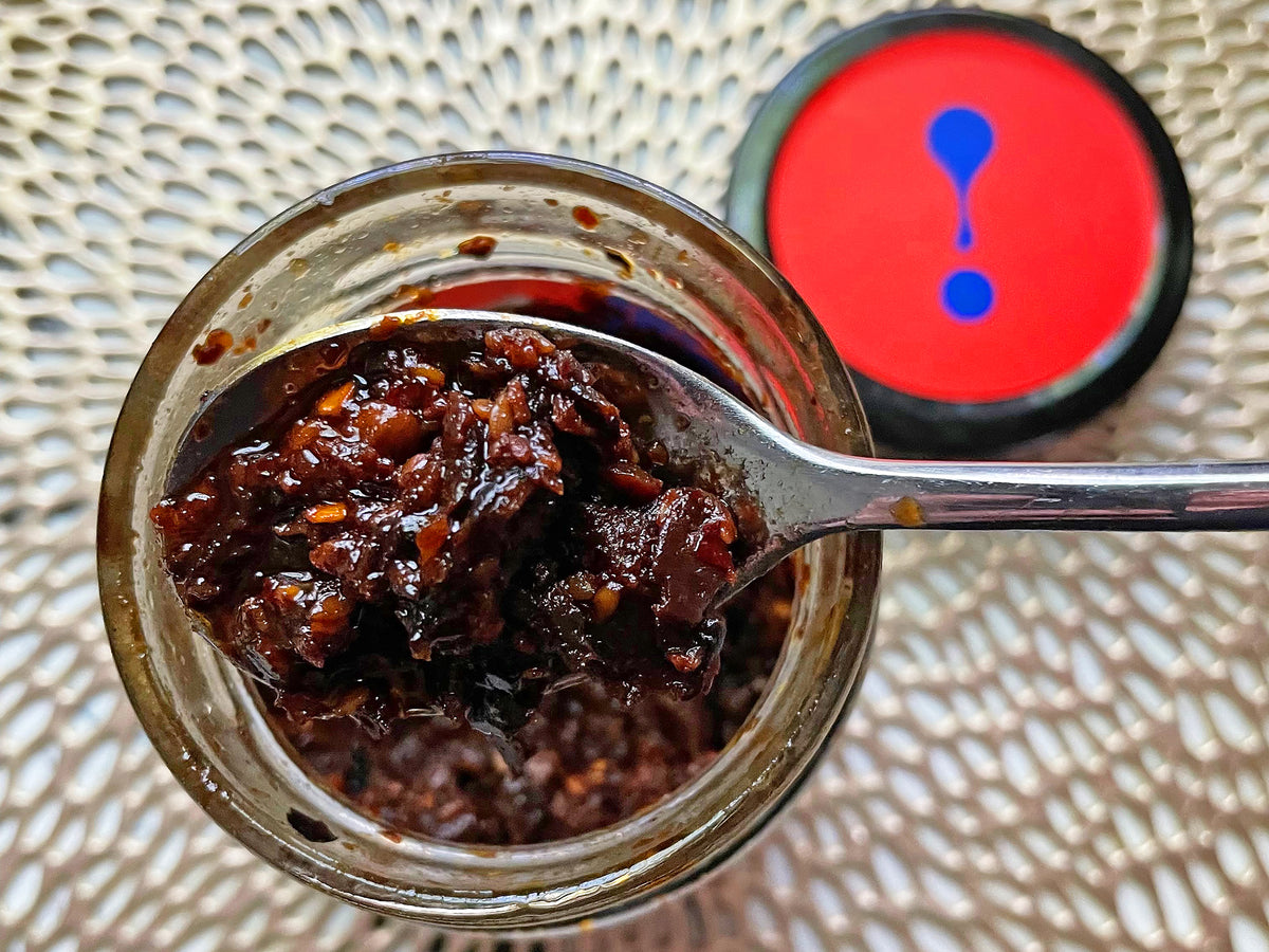 a jar of mushroom chili sauce with the top off and a spoonful of sauce resting on the top 