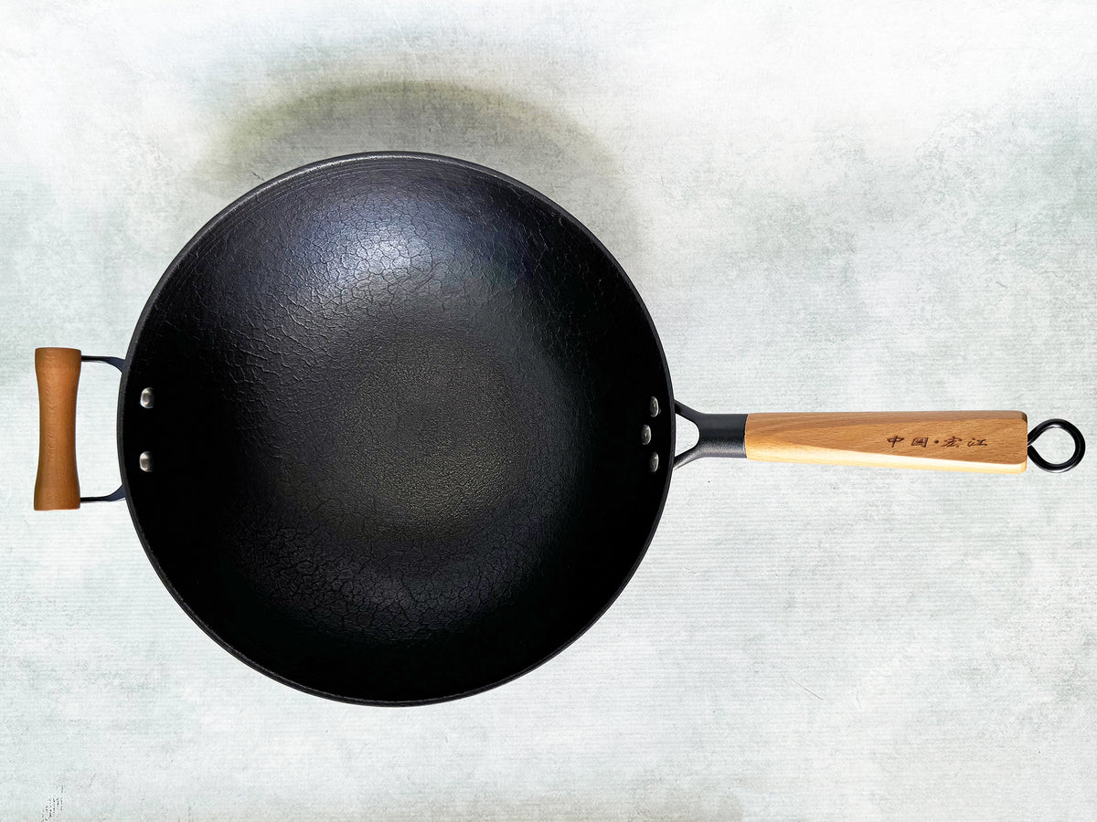 A top view of a 13.5-inch flat-bottom cast iron wok, showing the wok's diameter and the wooden handle.