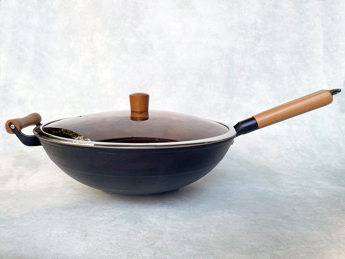 A 14.5-inch round-bottom cast iron wok with a glass lid and wooden handle