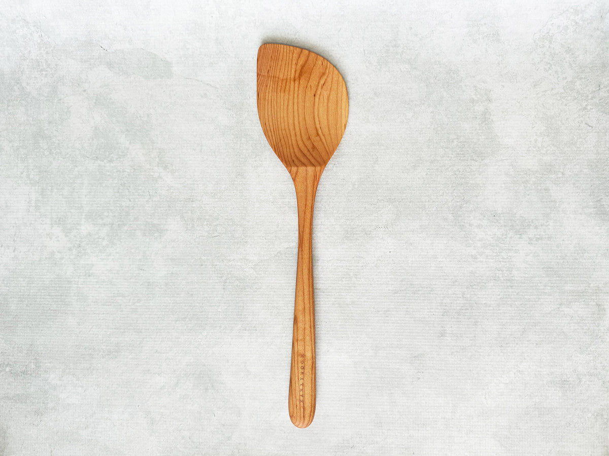 A large handcrafted wooden wok spatula angled to the left for a left-handed person
