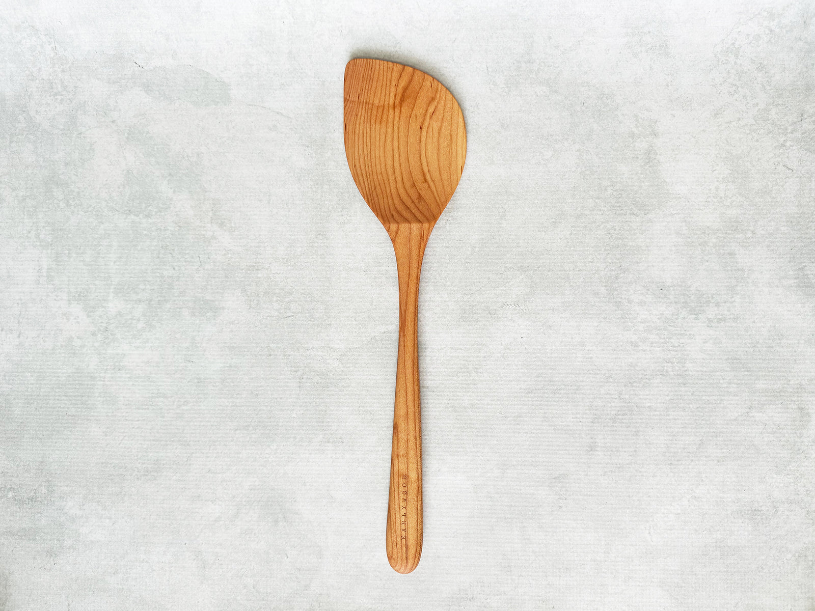 A large handcrafted wooden wok spatula angled to the left for a left-handed person