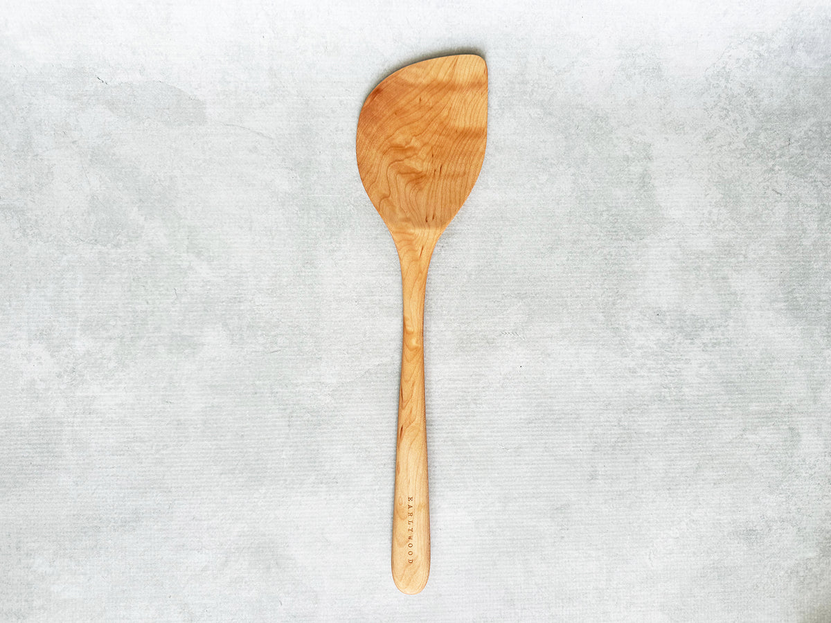 A large handcrafted wooden wok spatula angled to the right for a right-handed person