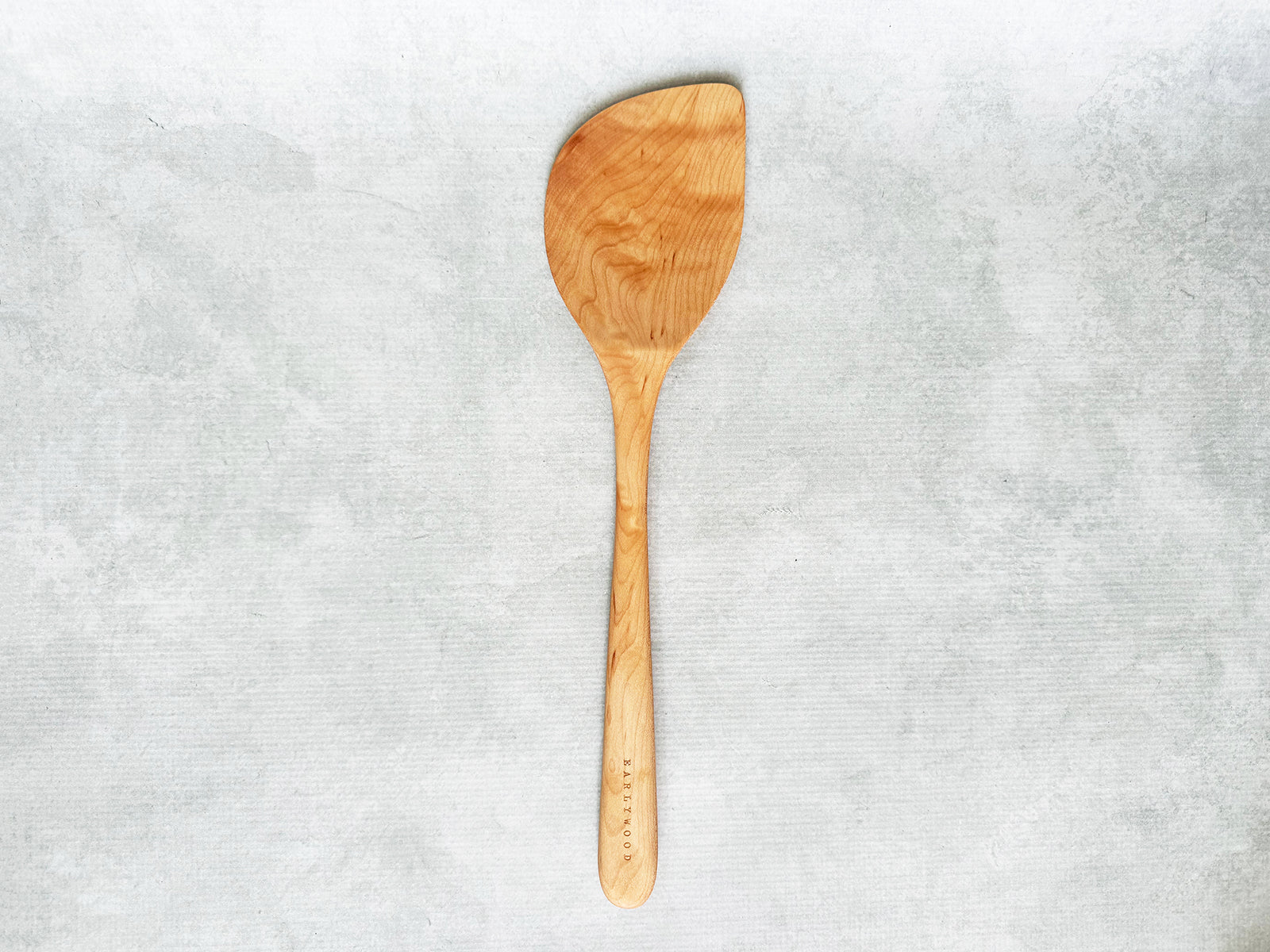 A large handcrafted wooden wok spatula angled to the right for a right-handed person
