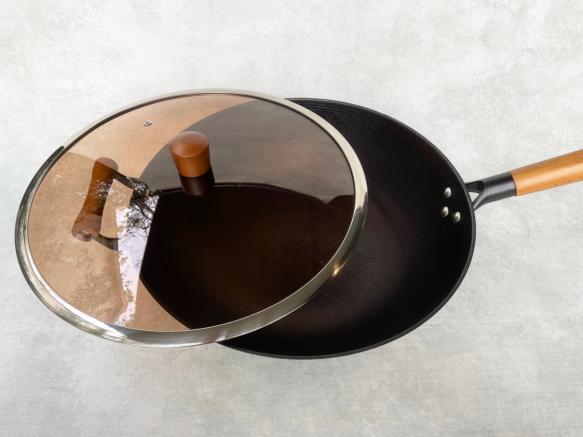 black cast iron wok shown with a smoked-glass lid