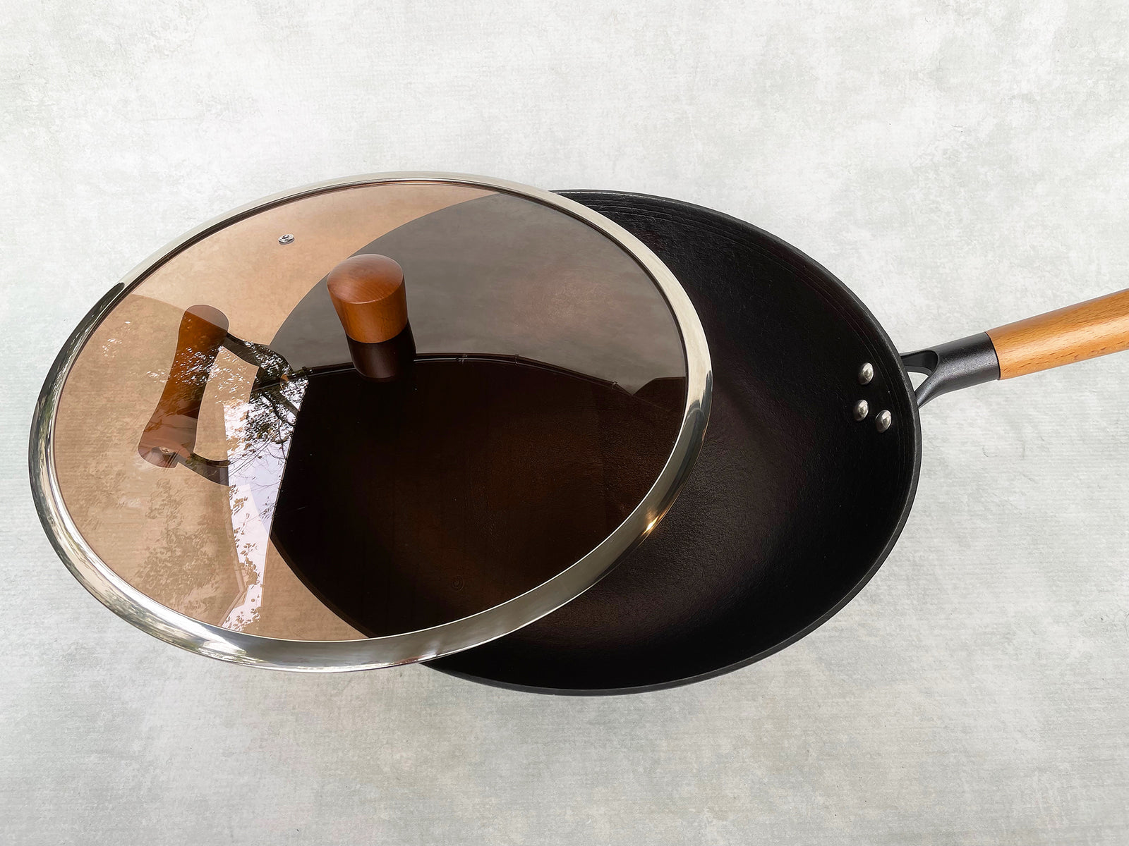 black cast iron wok shown with a smoked-glass lid