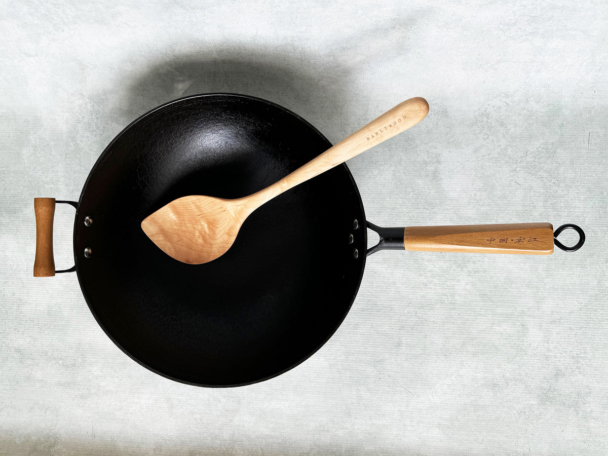 a black cast-iron wok with a wood wok spatula resting in it