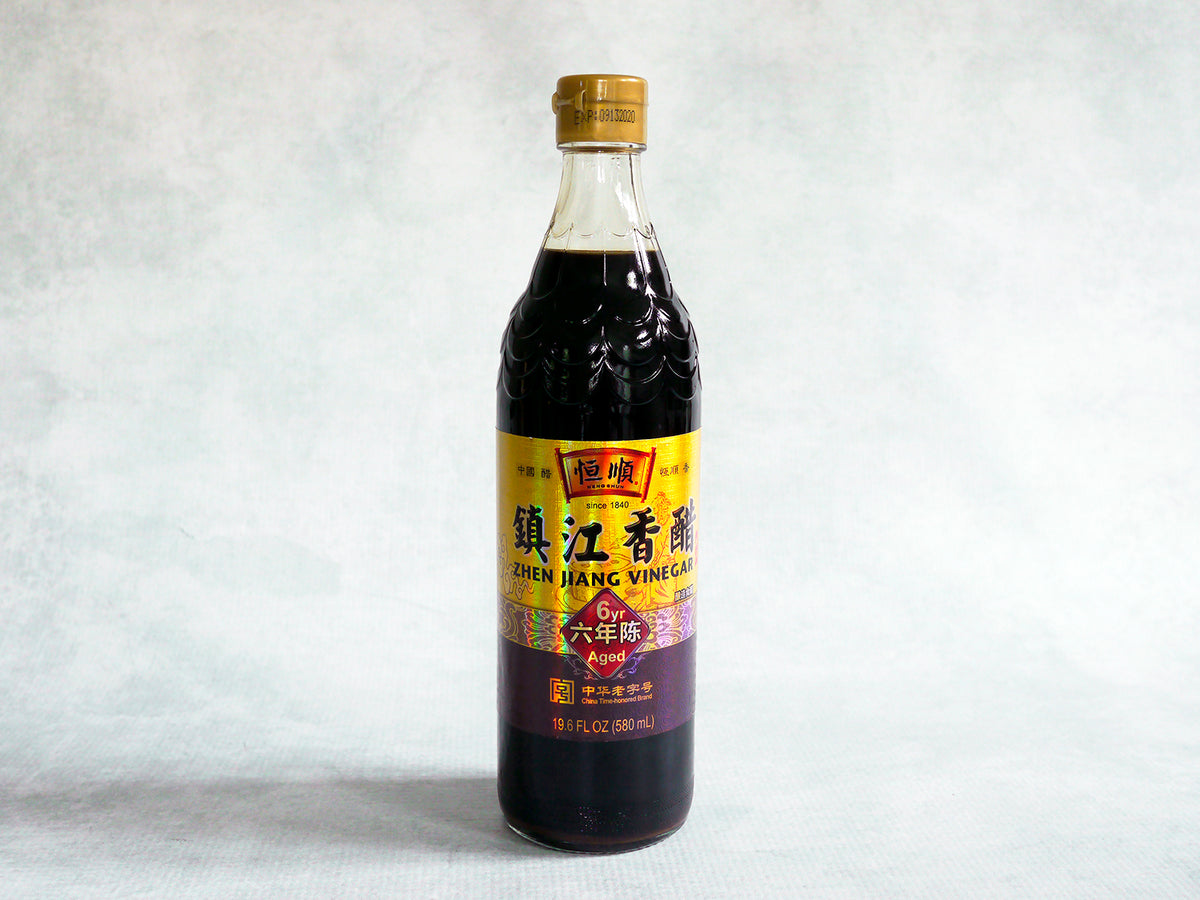 a glass bottle of black vinegar with a scalloped top and a gold label
