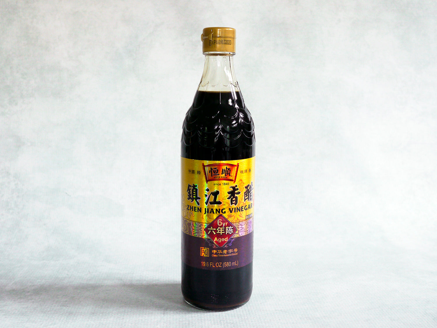 a glass bottle of black vinegar with a scalloped top and a gold label