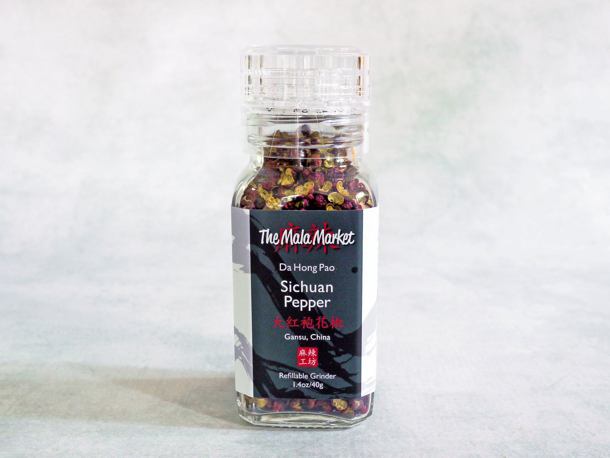 red Sichuan peppercorns inside a glass jar with a clear acrylic grinder top