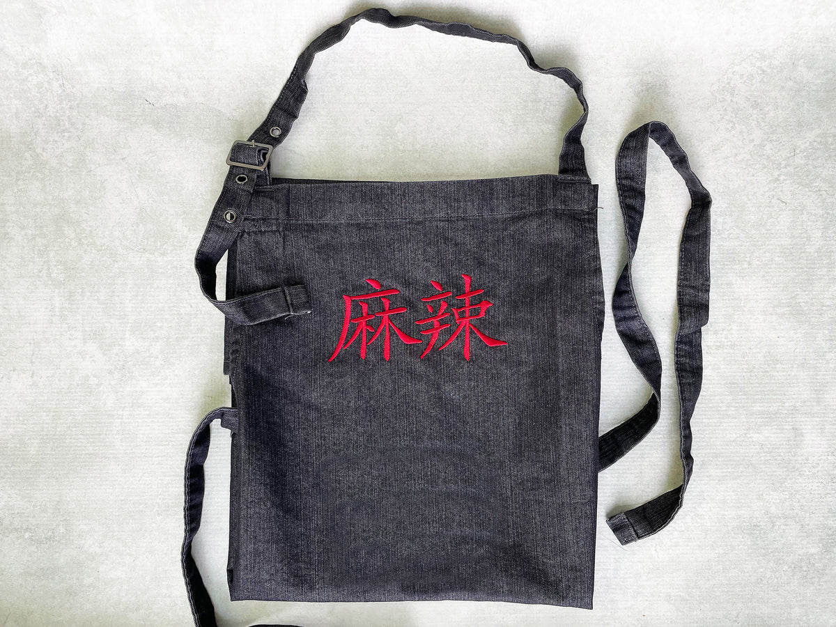 a dark gray cotton apron with the Chinese characters for mala embroidered on the top front in red