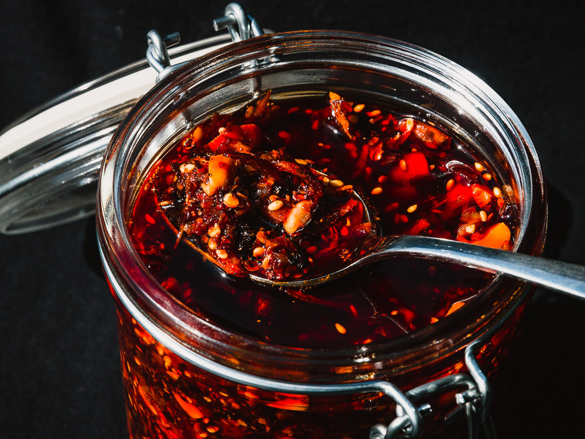 a glass jar of red chili crisp with the top open and a spoonful of crisp resting on top