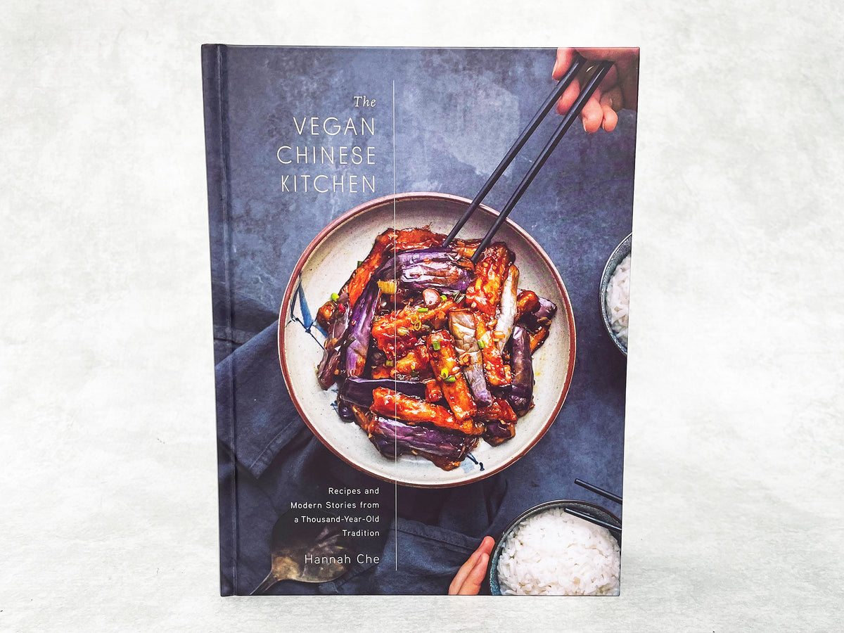 A hardcover copy of the cookbook The Vegan Chinese Kitchen by Hannah Che, showing a dish of cooked eggplant