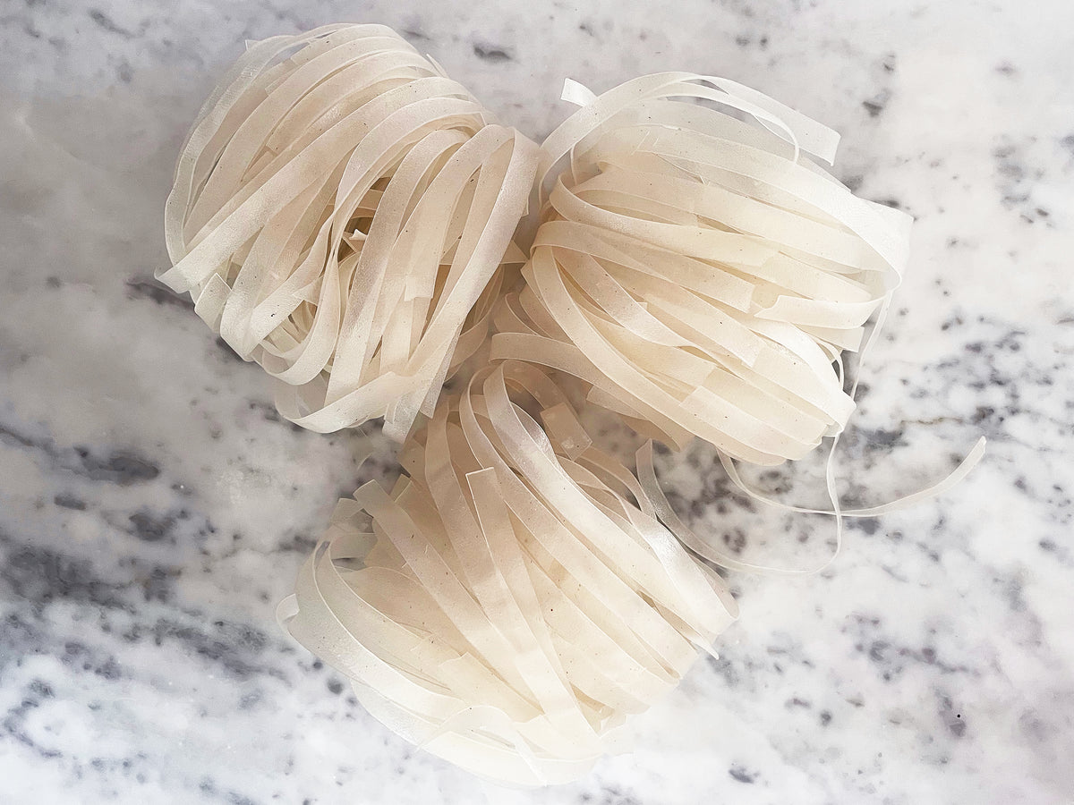 three bundles of dried wide rice noodles for making chow fun sitting on a counter