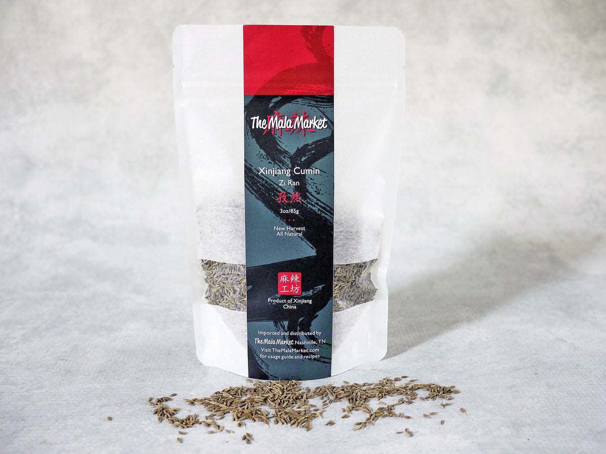 a scattering of tan cumin seeds grown in Xinjiang is shown in front of a white kraft bag
