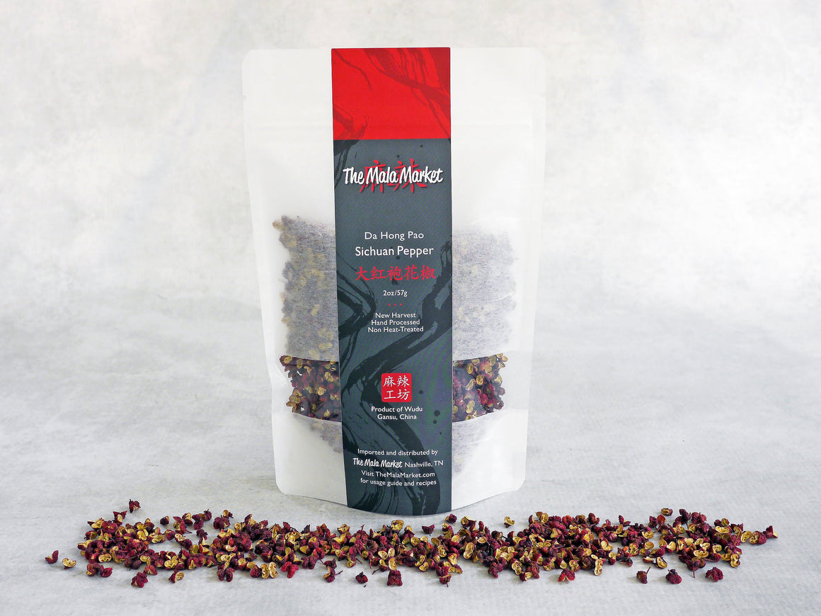 a white kraft bag of Sichuan peppercorns with the loose red peppercorns also displayed in front of the bag