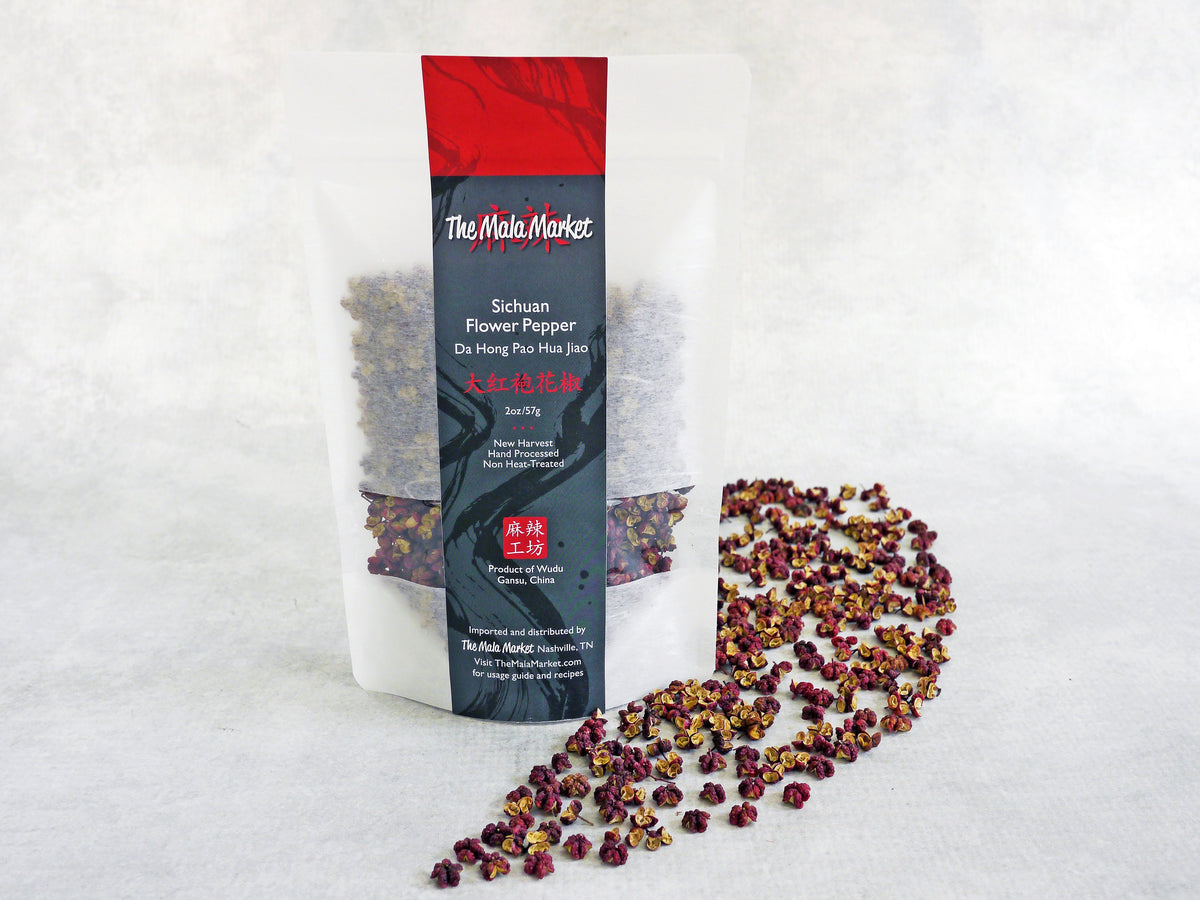 large Sichuan peppercorns are shown fully opened into three parts, red on the outside and yellow on the inside, with no seeds, displayed in front of their white kraft bag
