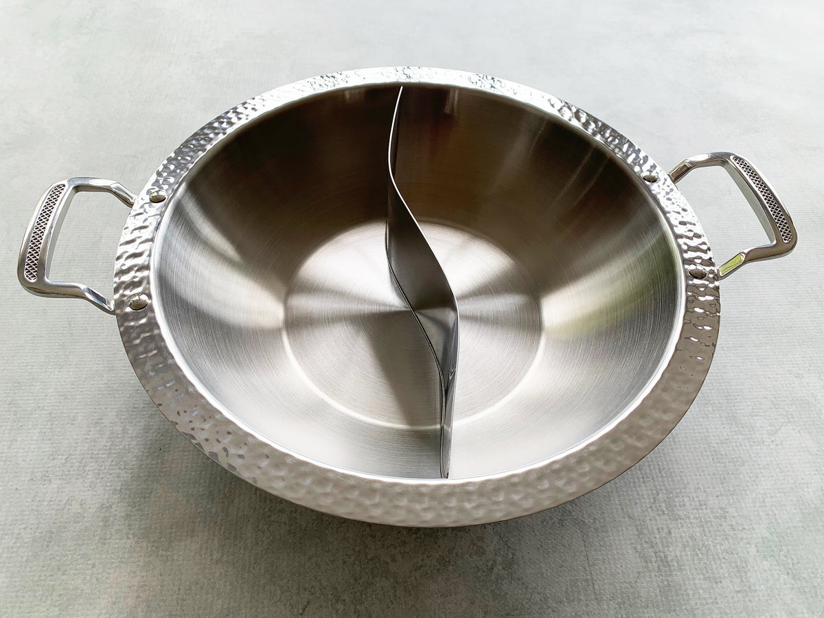 a side view of a stainless steel hot pot with a hammered-steel edge, brushed steel interior, and patterned steel handles